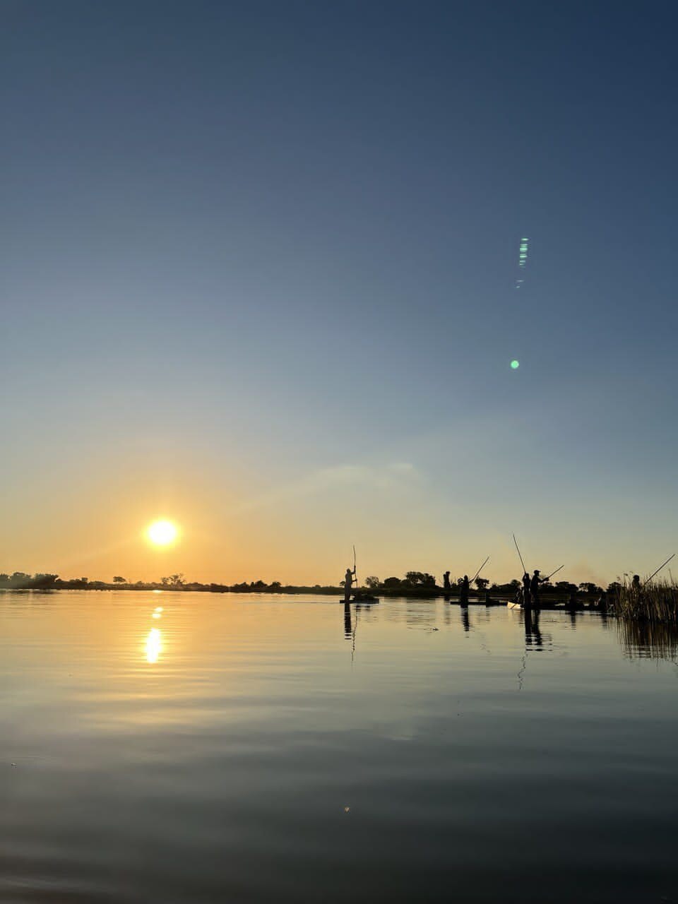 Local mokoro polers guiding guests across the Okavango Delta at sunset